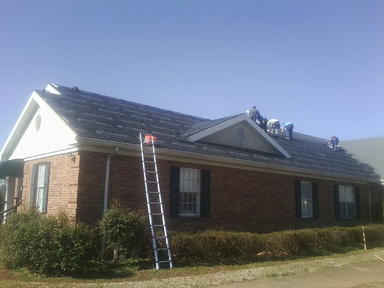 Crew tearing shingles off a brick ranch roof with a ladder set — Metal Roof Repair work by our crew in Okeana
