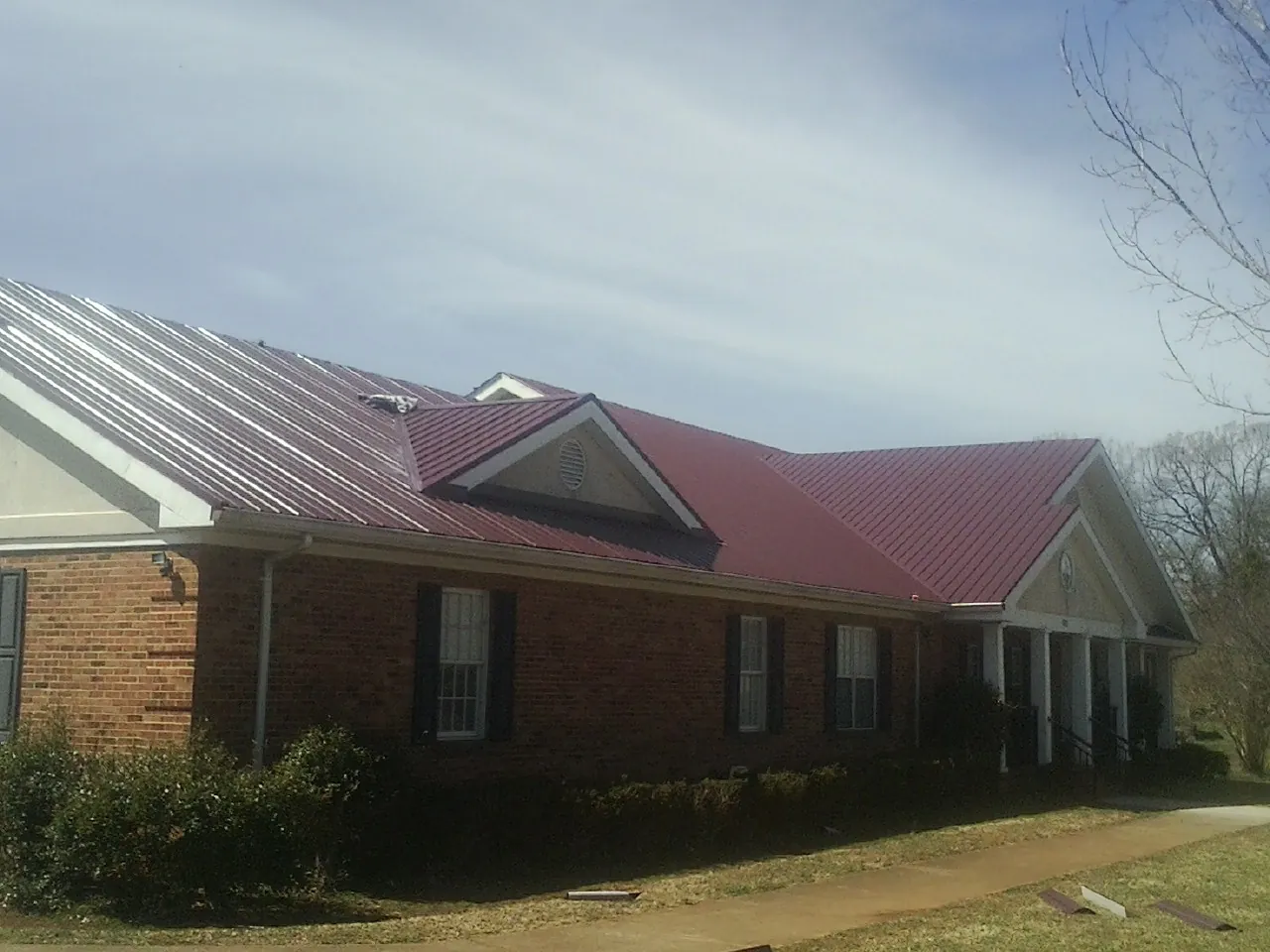 Red metal roof with gabled entries on a long brick building, from a Hail Damage Roof Repair job in Okeana
