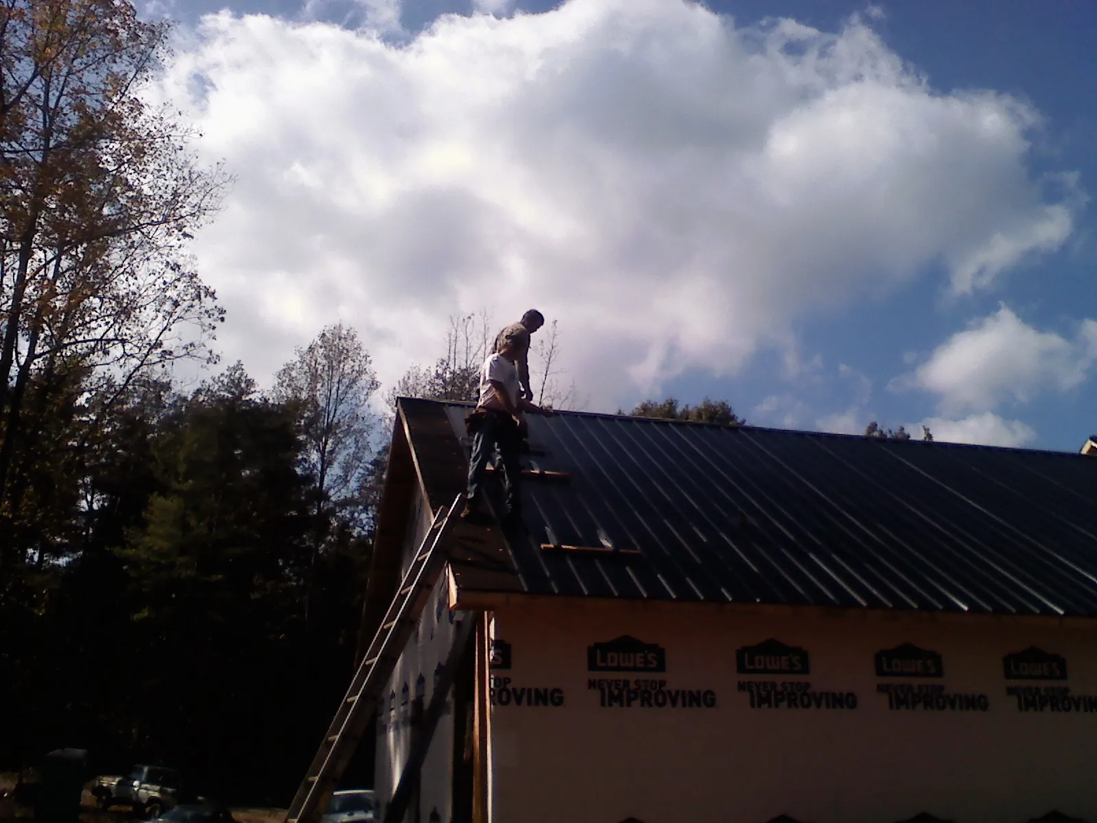 Roofer fastening dark metal panels high against a cloudy sky, from a Roof Inspection job in Okeana