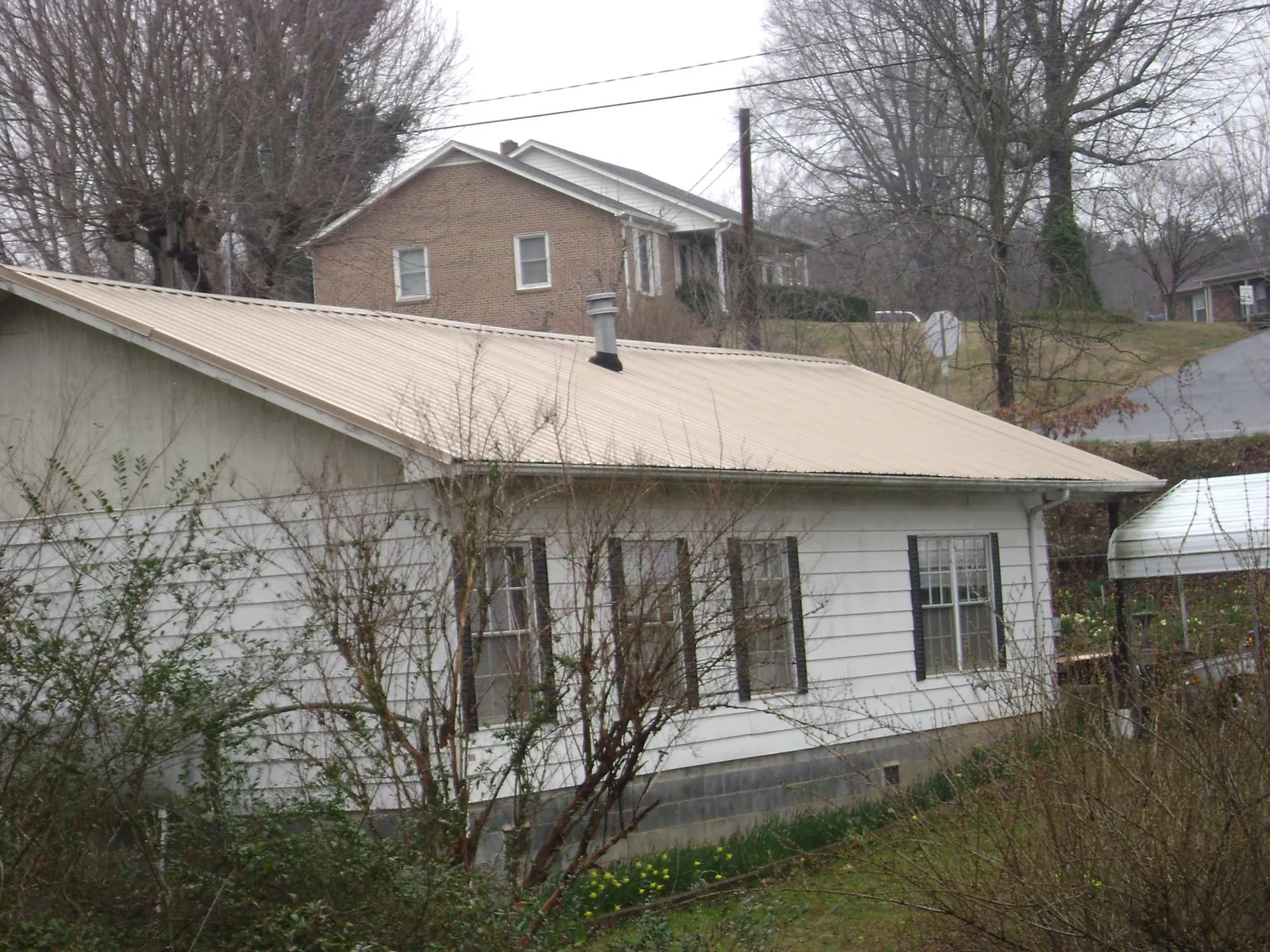 Tan metal roof on a white sided house set into a hillside — Commercial Roofing by Roofing Brothers in Okeana