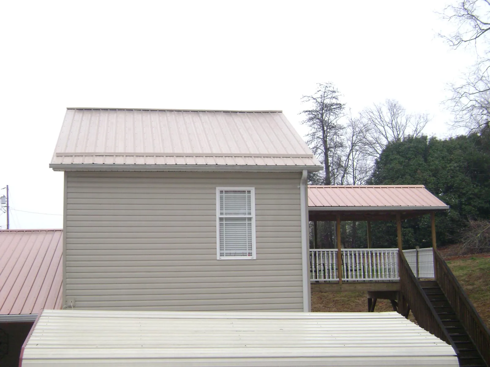 Tan metal roofs on a two story addition and attached porch, from a Roof Replacement job in Okeana